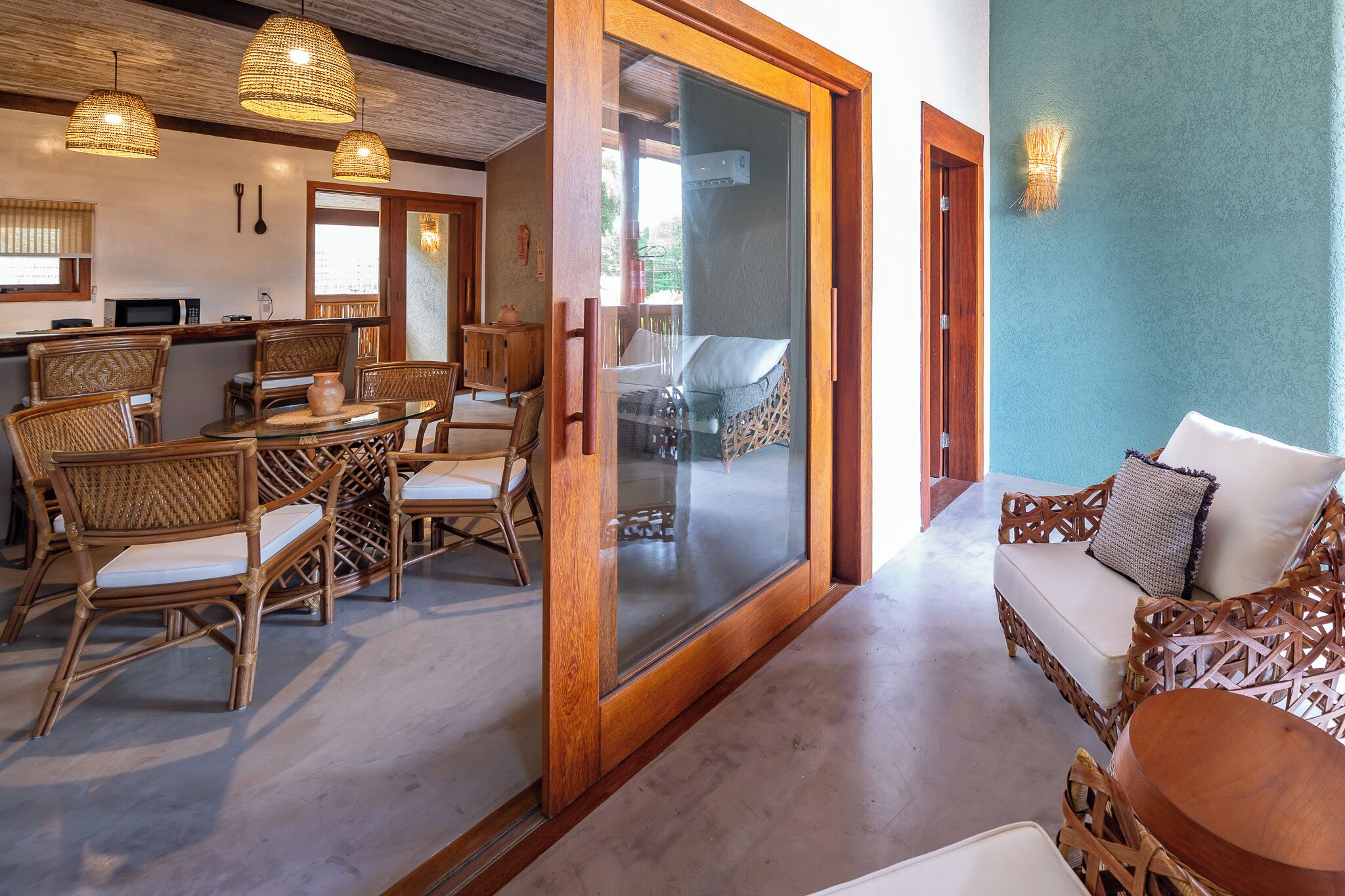 A room with a dining area, a sofa, wicker furniture, and a glass door leading outside.