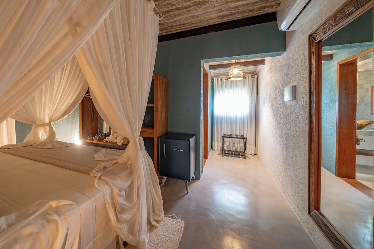 A bedroom with a canopy bed, a small cabinet, and a mirror.
