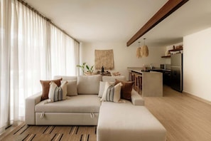 Una sala de estar con sofá, reposapiés y una zona de cocina con refrigerador y lavaplatos.