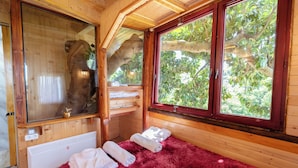 A wooden cabin with a large window, a red furry rug, and towels on the floor.