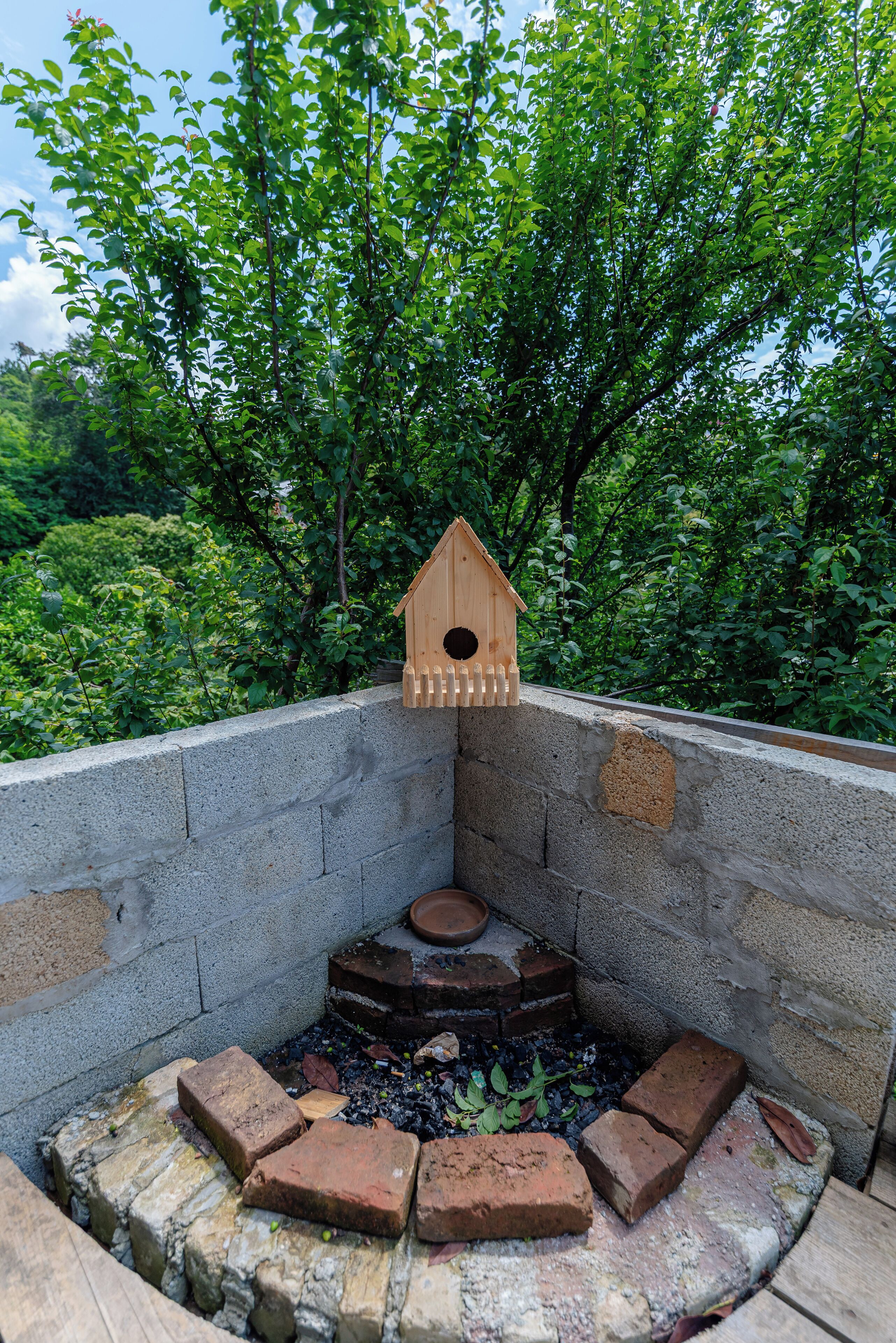 A birdhouse mounted on a brick wall with a surrounding brick seating area.