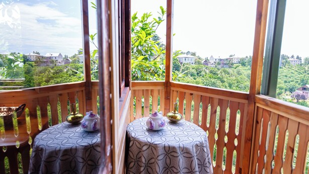 A wooden gazebo with two tables, each with a patterned tablecloth and a teapot, overlooking a lush landscape.