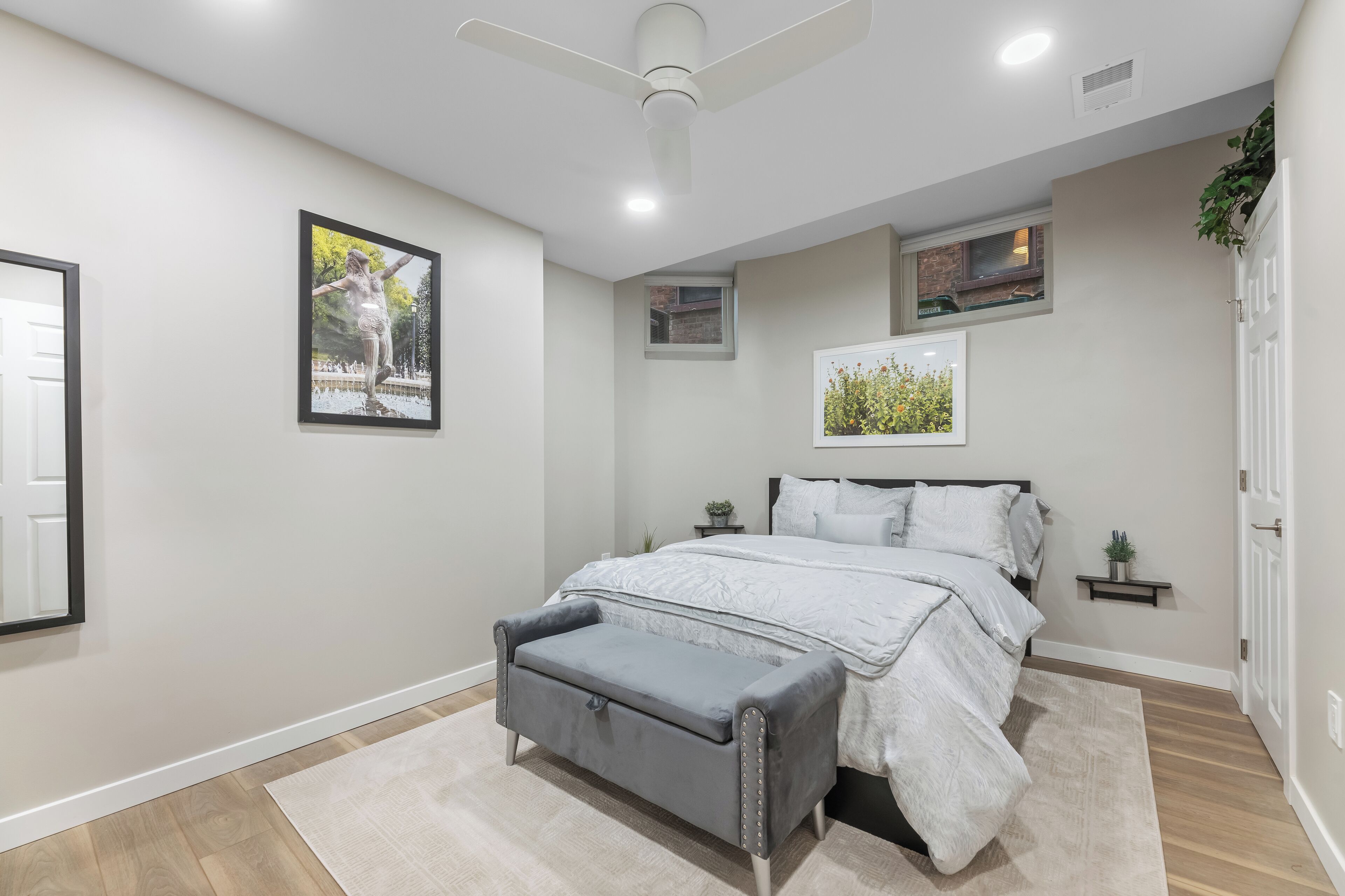 A bedroom with a bed, a bench, a ceiling fan, and framed pictures on the wall.