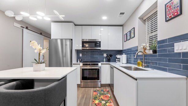Una cocina moderna con armarios blancos, electrodomésticos de acero inoxidable y un salpicadero de azulejos azules.