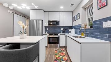 A modern kitchen with white cabinets, stainless steel appliances, and a blue-tiled backsplash.