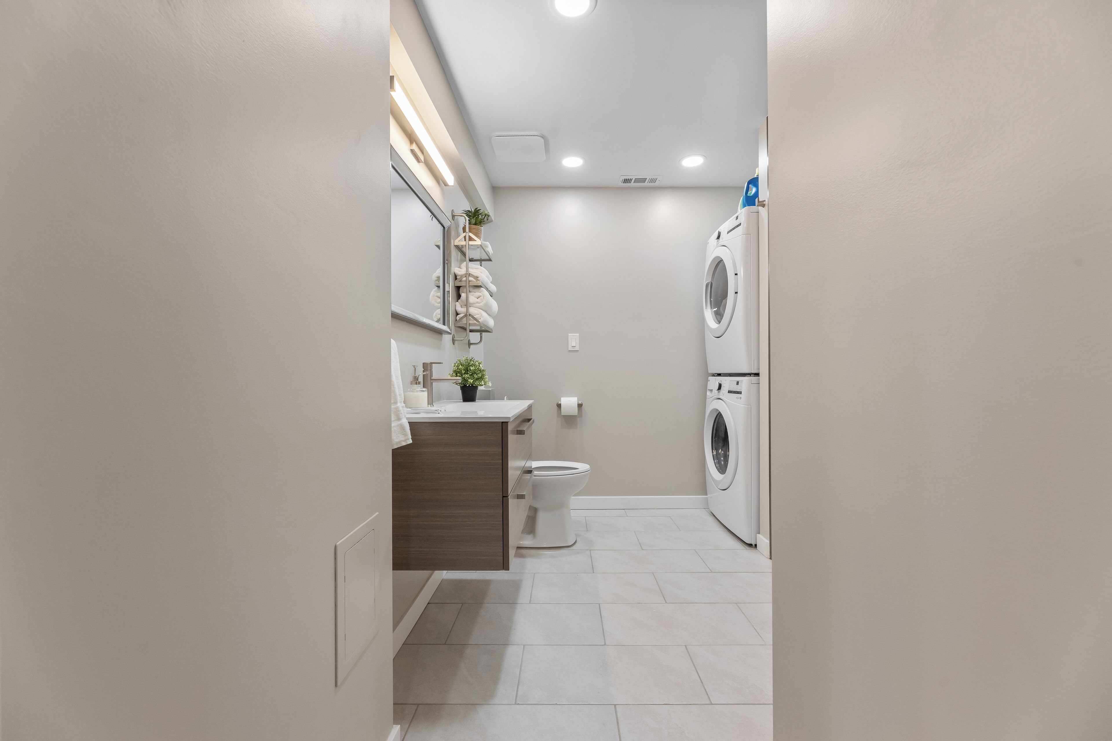 Ein modernes Badezimmer mit Toilette, Waschbecken und übereinander angeordneter Wasch- und Trockenmaschine.