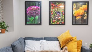 Una sala moderna con un sofá gris, una manta color crema y tres cuadros florales en la pared.