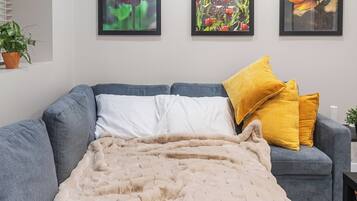 A modern living room with a grey sofa, a beige blanket, and three framed floral artworks on the wall.