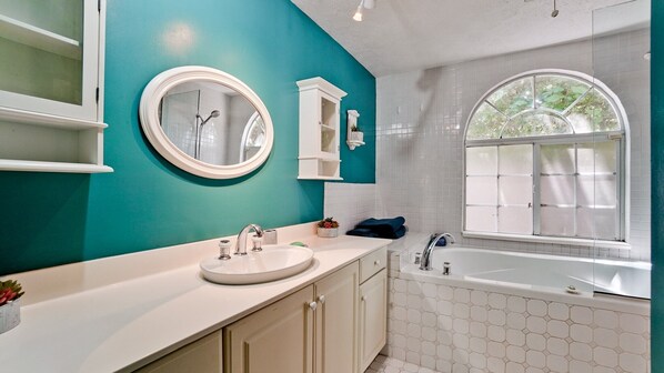 Une salle de bain avec un lavabo blanc, une baignoire, une fenêtre et un miroir.