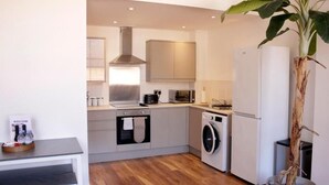 Una cocina compacta con electrodomésticos modernos, lavadora y una planta en maceta.