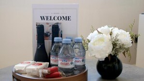 Un letrero de bienvenida, agua embotellada, refrigerios y un jarrón con flores sobre una mesa.