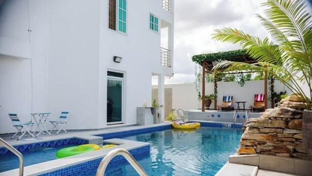 A swimming pool with a blue tiled edge, a stone wall, and a pergola with plants. - Peaceful Escape in Tema Community 25 (Dawhenya)