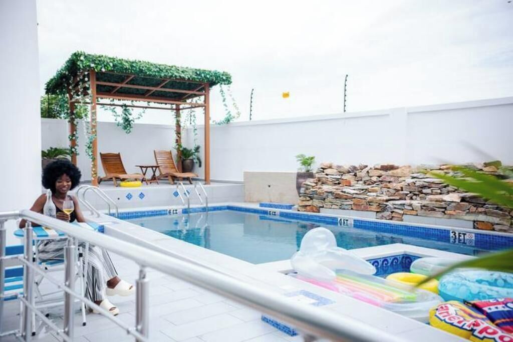 An indoor swimming pool with a stone wall, a wooden pergola with greenery, and lounge chairs.