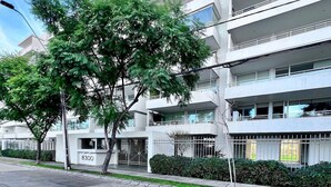 A multi-story building with balconies, a parking lot, and a street with trees. - Moderno y equipado estudio en Los Dominicos (Santiago)