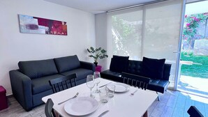 A modern living space with a dining area, a sofa, and a large window. - Moderno y equipado estudio en Los Dominicos (Santiago)