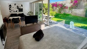 A modern bedroom with a large bed, a TV, a desk, and a balcony with a garden view. - Moderno y equipado estudio en Los Dominicos (Santiago)