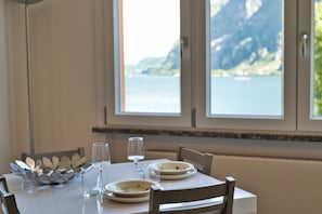 Mesa de comedor con platos, vasos y cubiertos, con vistas a una ventana que muestra un lago y montañas.