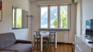 Una habitación con sofá, mesa de comedor con sillas, televisor y ventana con vista a la montaña.