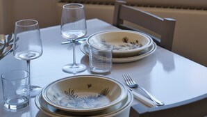 Una mesa de comedor con platos, vasos y cubiertos, frente a una ventana con vista a un cuerpo de agua y montañas.