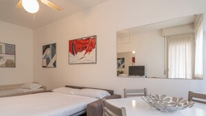 Una habitación de hotel con dos camas, una mesa de comedor y un cuenco decorativo, un televisor y obras de arte en las paredes.