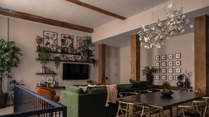 A modern living room with a green sofa, a dining table with chairs, a TV mounted on the wall, and various plants and decorations. - The Artisan's Duplex - 8Bd/5.5Bth w/2 Car Parking! (Philadelphia)
