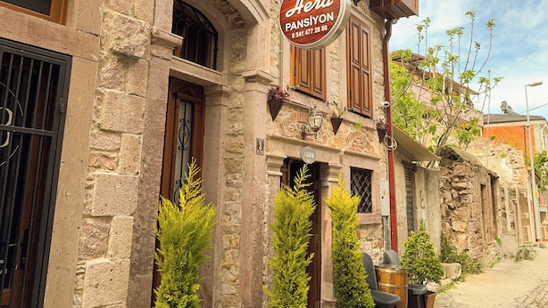 A stone building with a sign for "Hera Pansiyon" and a small outdoor seating area with potted plants. - Hera Pansiyon (Ayvalik)