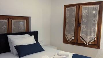 Una cama bien hecha con ropa de cama blanca y azul, un cabecero de madera y una ventana con cortinas de encaje.