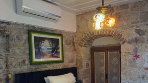 A bedroom with a bed, a painting, a stone wall, and a wooden door. - Hera Pansiyon (Ayvalik)