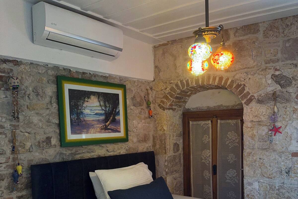 A bedroom with a bed, a painting, a stone wall, and a wooden door.