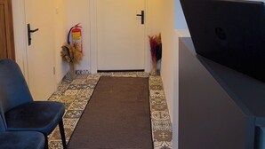 A hallway with patterned floor tiles, a door, a fire extinguisher, a wall-mounted light fixture, and a framed artwork. - Hera Pansiyon (Ayvalik)