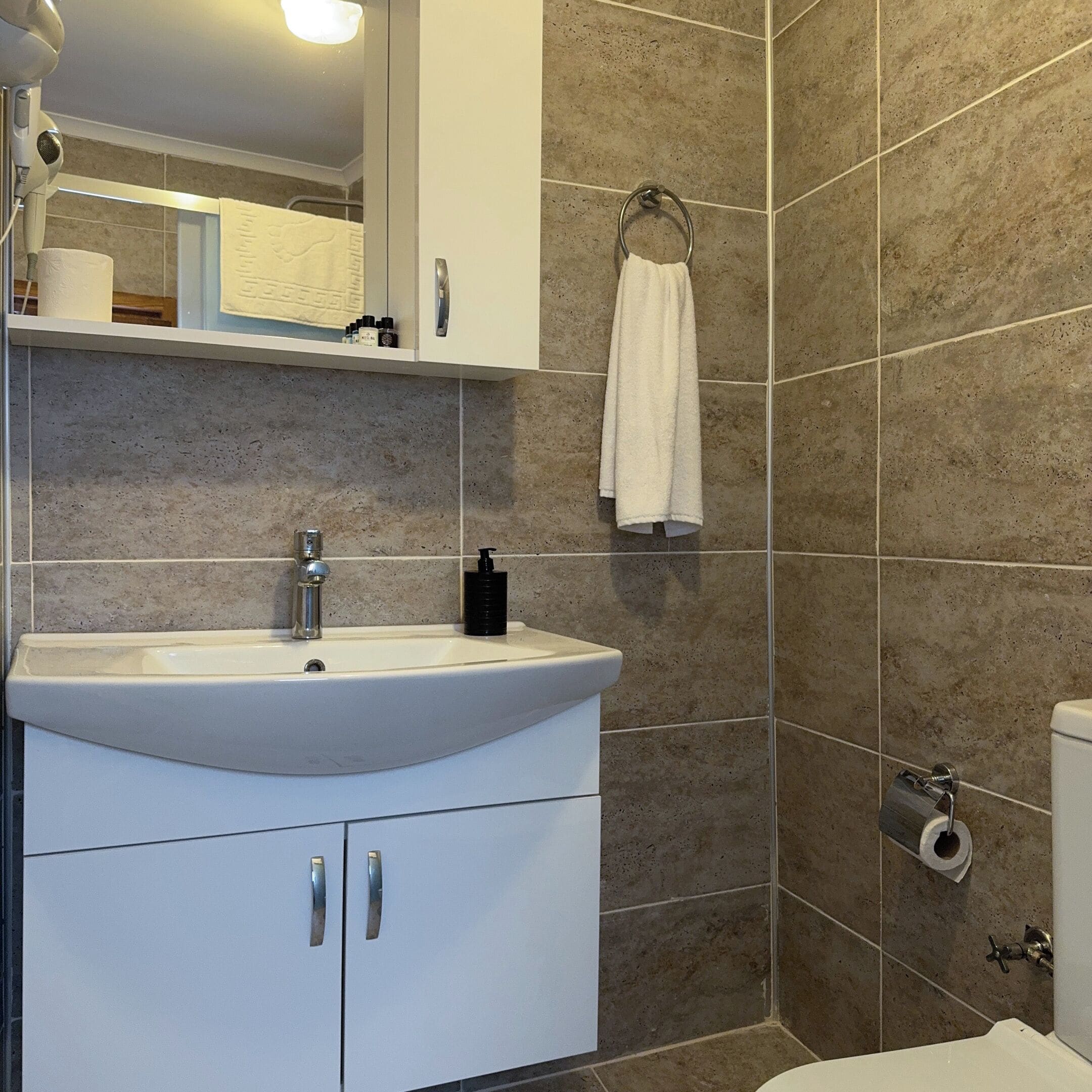 Ein Badezimmer mit weißem Waschbecken, einem Spiegel, einem Handtuchhalter und einer Toilette.