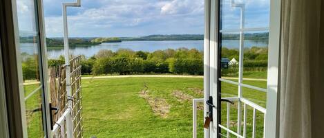 Blick von einem Balkon mit Glasdoor, auf eine Wiese und einen See.