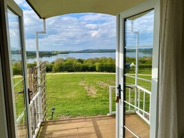 Vista de uma varanda com porta de vidro, com vista para uma área gramada e um lago.