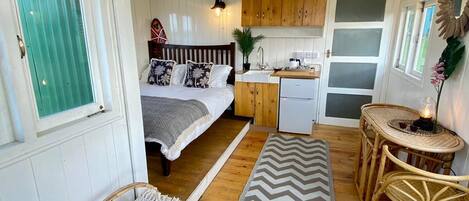 Une chambre de style cabane rustique et compacte, comprenant un lit, une petite kitchenette et un coin repas avec des meubles en osier.