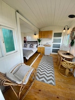 Quarto compacto e rústico em estilo cabana, com cama, pequena cozinha e área de jantar com móveis de vime.
