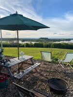 Un montaje para picnic con una mesa, sillas y una parrilla, con vista a un lago y campos de césped.