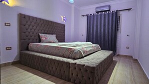 A bedroom with a large bed, a bench, a ceiling fan, and a window with curtains.