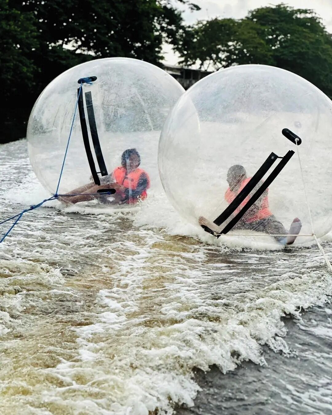 Dos personas dentro de esferas transparentes deslizándose sobre el agua.