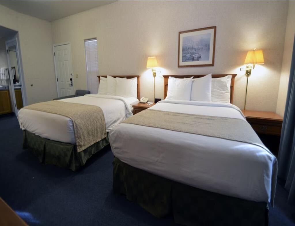 A hotel room with two beds, a desk, a chair, and two bedside lamps.