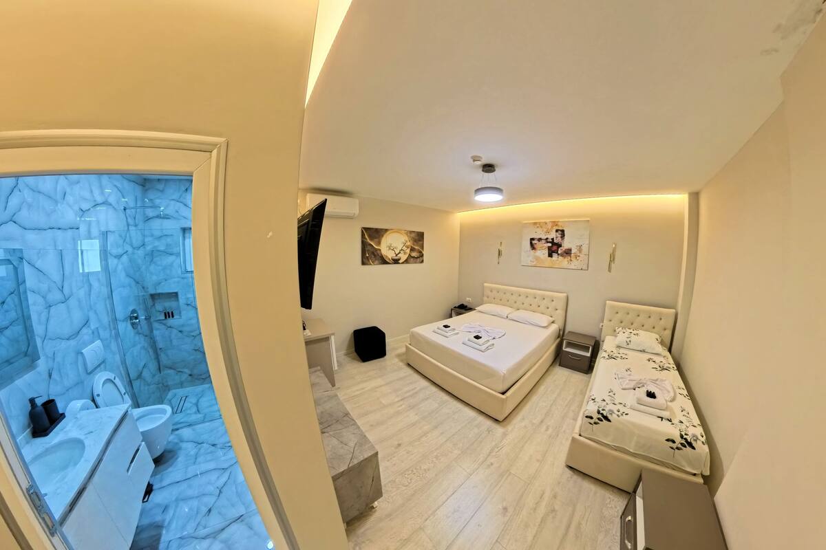 Un dormitorio con baño de mármol, una cama con cabecera y una mesita de noche.