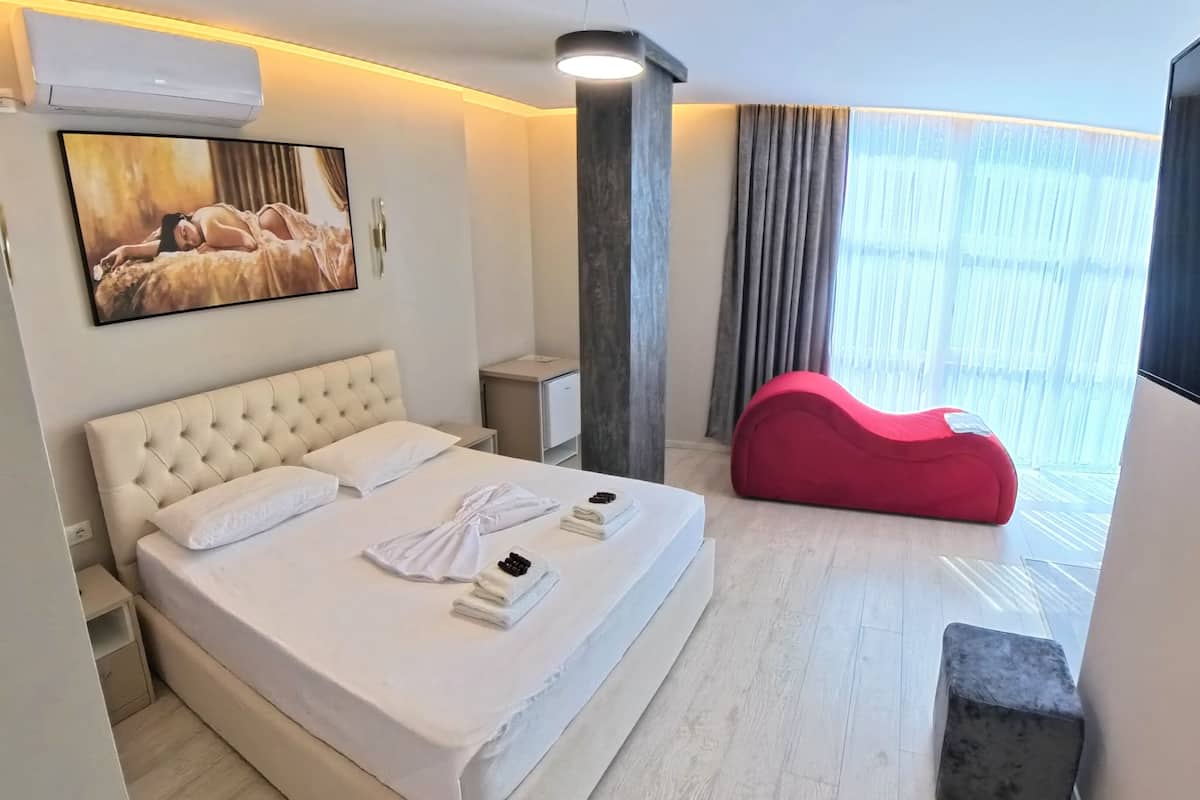 Habitación de hotel con cama, un sillón de peluche rojo, un televisor de pantalla plana y un cuadro en la pared.