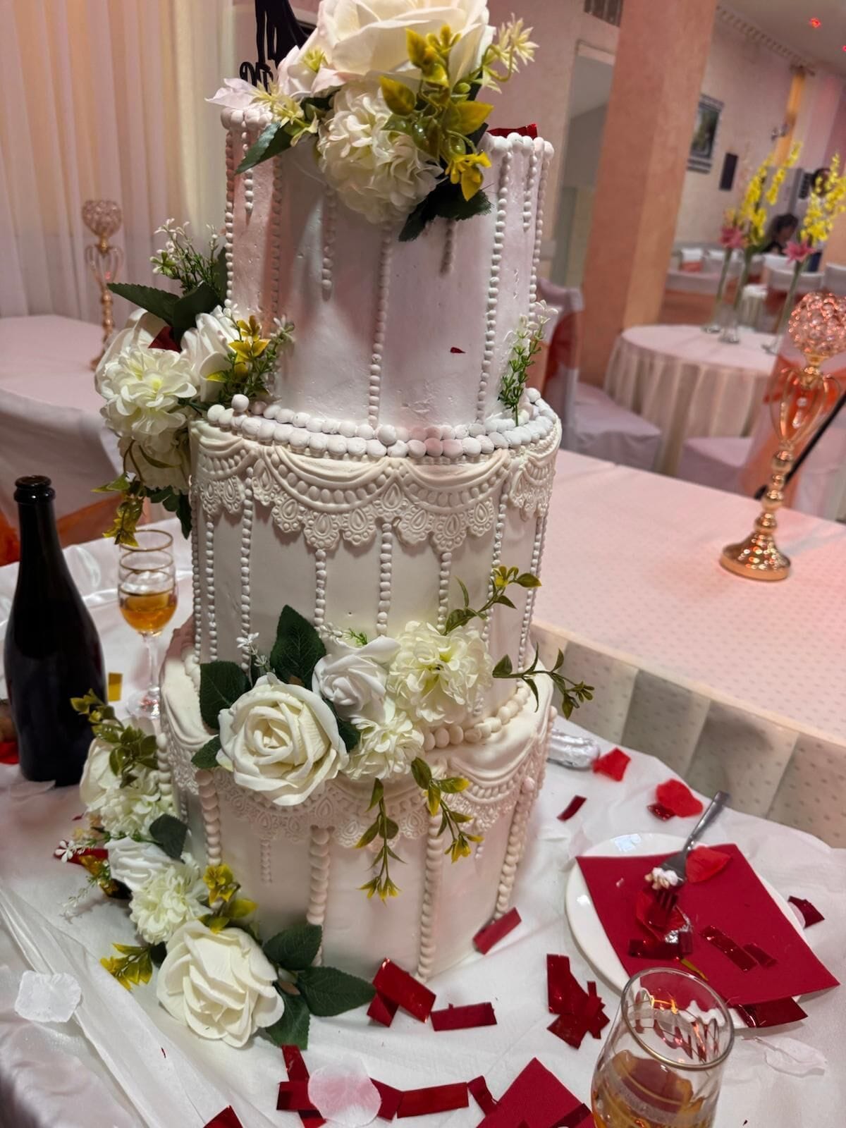 A multi-tiered cake with white icing and floral decorations, placed on a table with a white tablecloth.