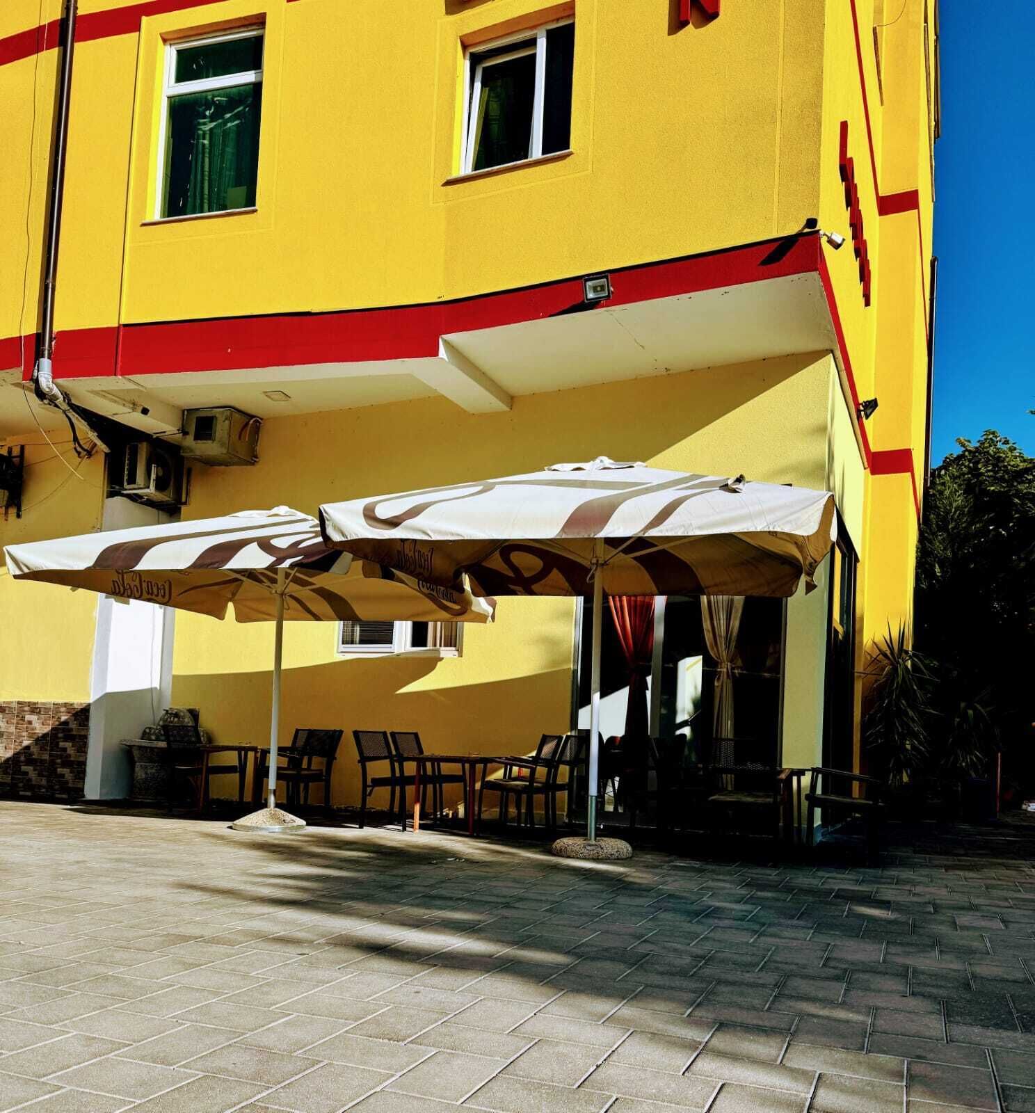 A yellow building with a red awning, outdoor seating, and a tiled patio.