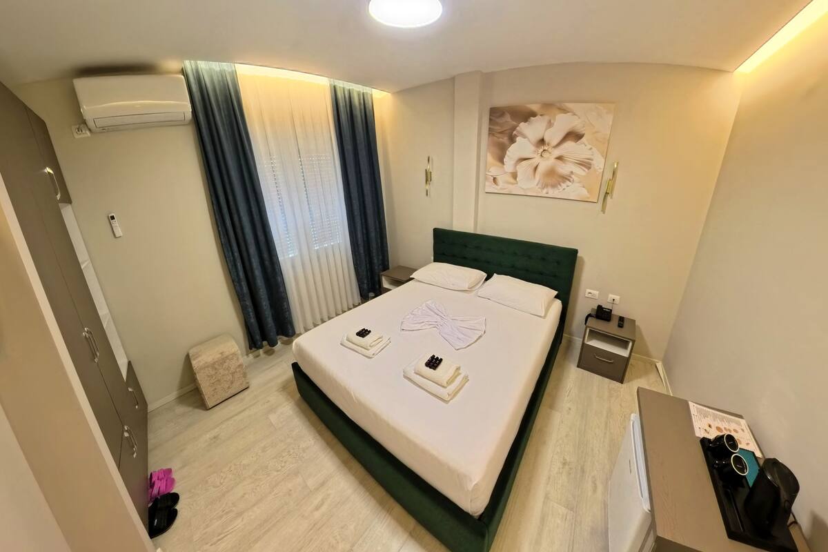 Habitación de hotel con cama, mesita de noche y aire acondicionado instalado en la pared.