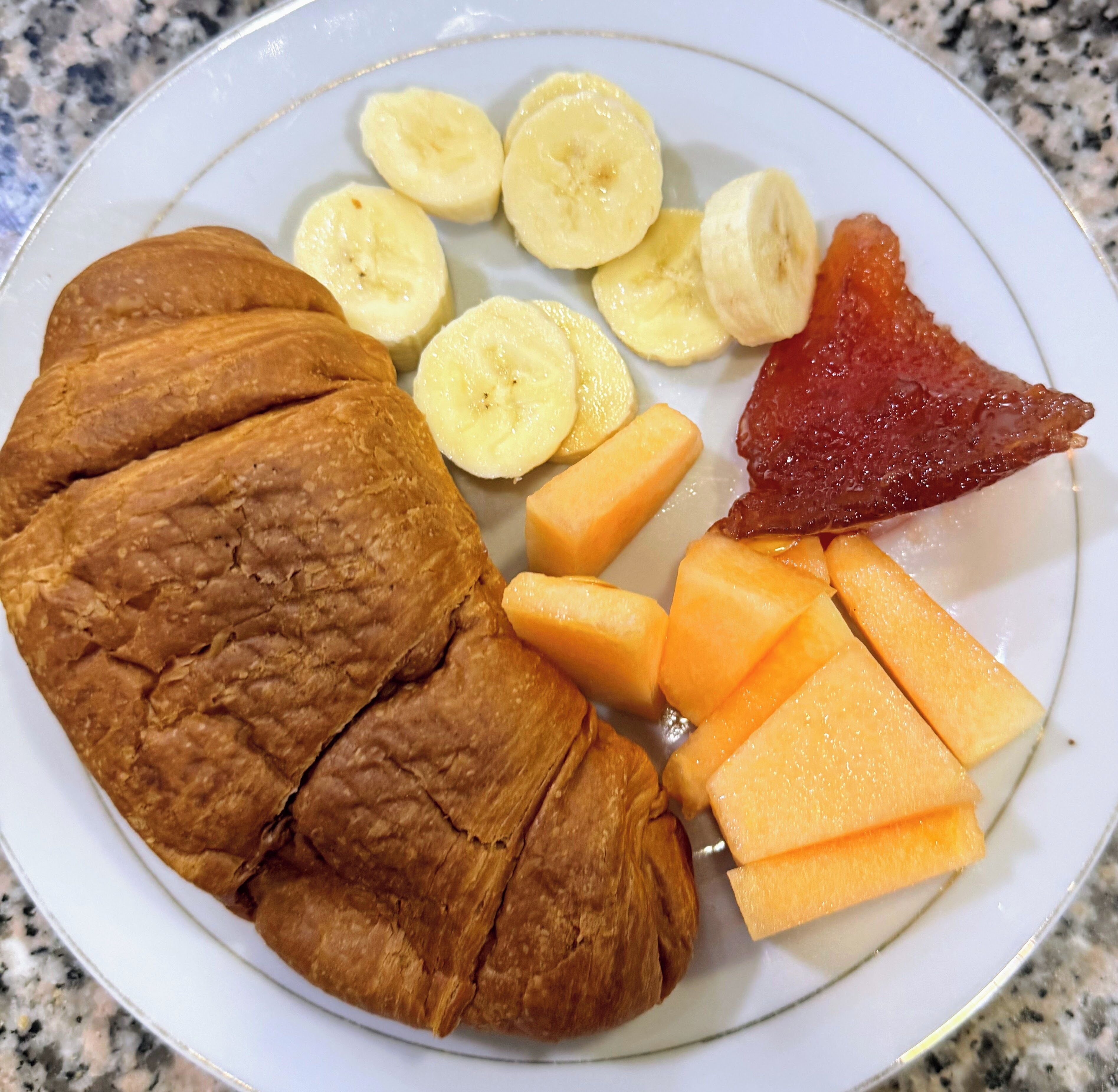 A plate with sliced bananas, cantaloupe, and a piece of meat.