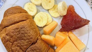 A plate with sliced bananas, cantaloupe, and a piece of meat.