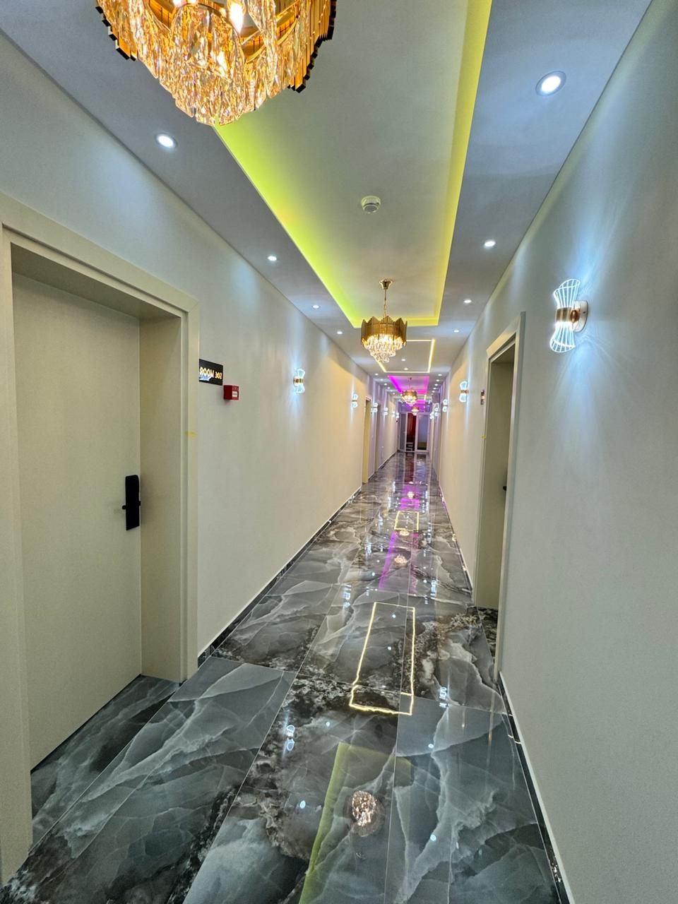 Un pasillo con piso de mármol, iluminación empotrada y un candelabro.