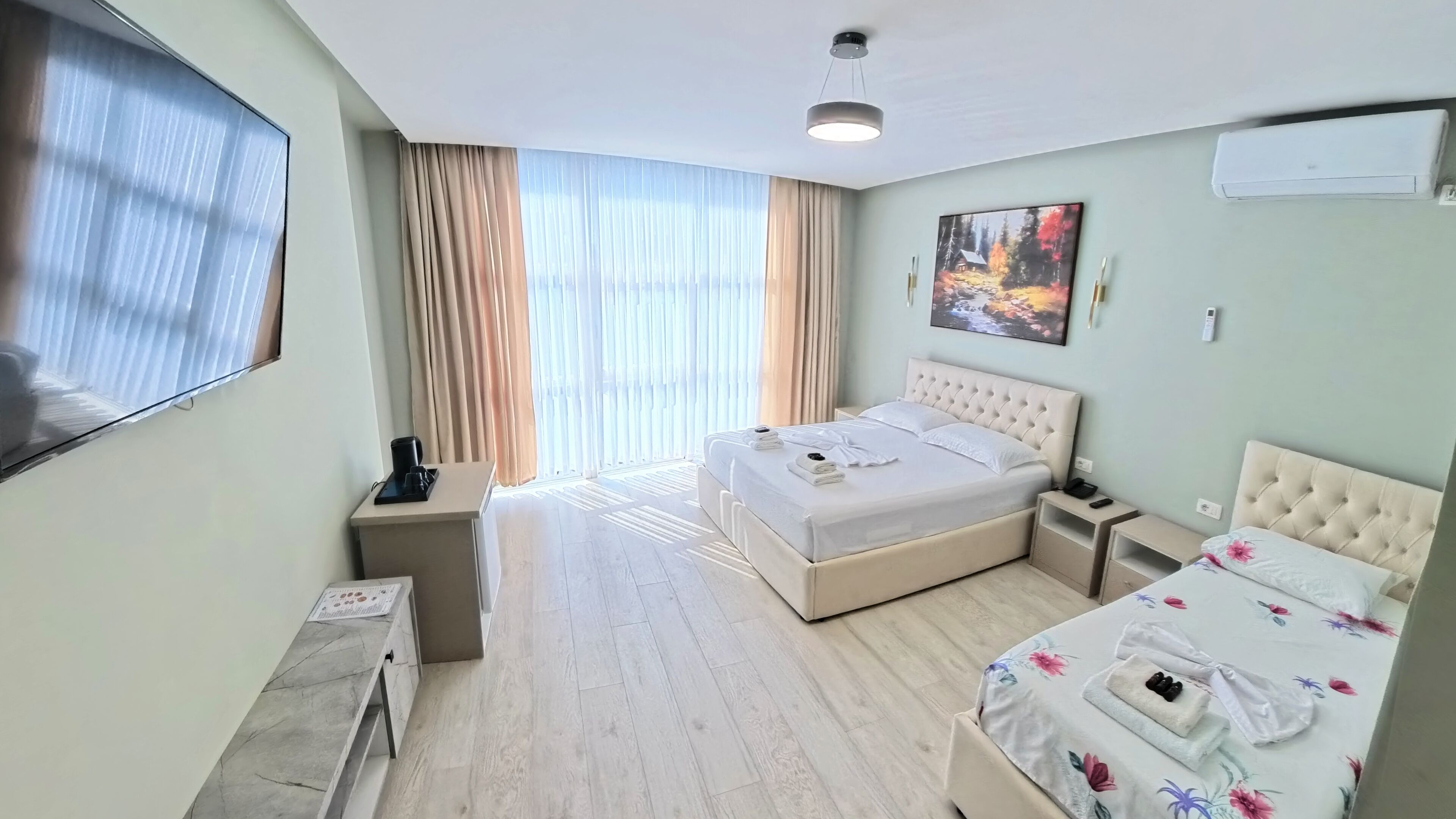 Hotellihuone, jossa on suuri sänky, yöpöytä, työpöytä, tuoli, litteänäyttöinen televisio ja ikkuna, jossa on verhot.