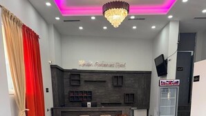 A restaurant interior with a reception desk, multiple tables and chairs, and a modern chandelier. - London Restaurant Hotel (Kukës)