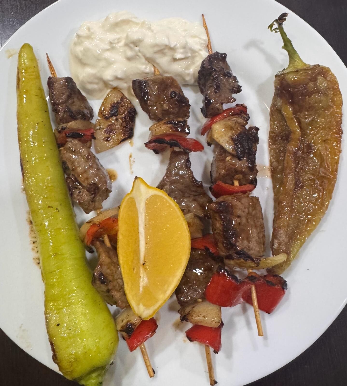 Un plato con brochetas de carne a la parrilla, un pimiento asado y un gajo de limón.